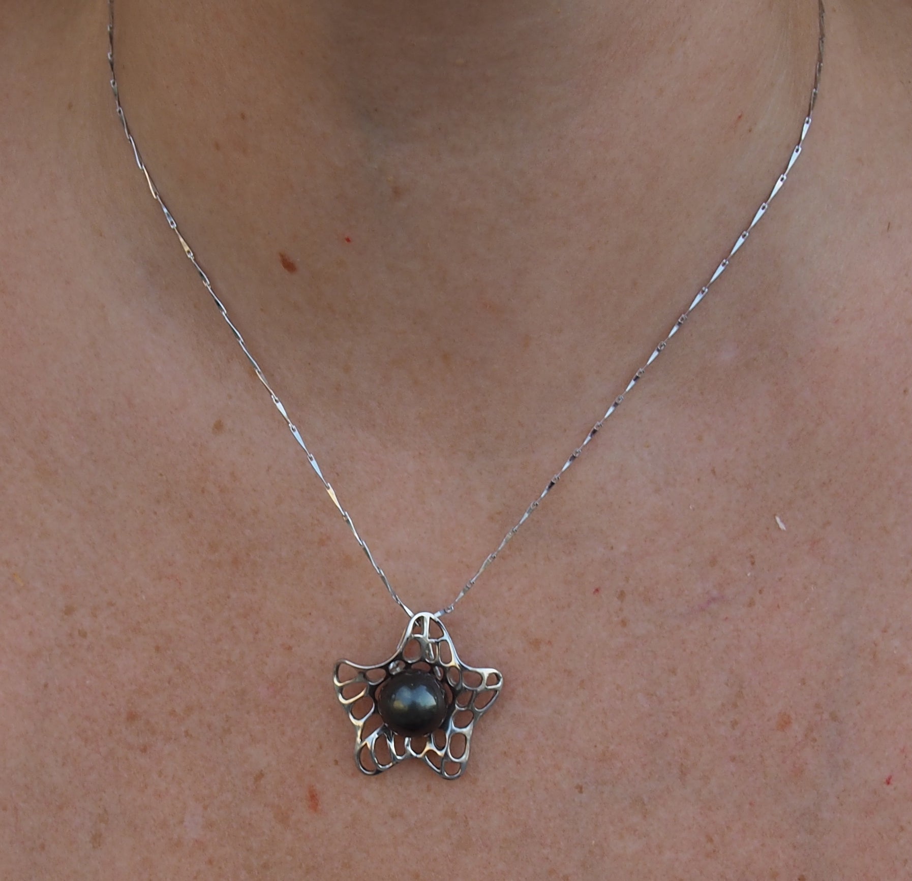 Collier fleur argent 925 orné d'une perle de Tahiti noire présenté sur nacre polynésienne